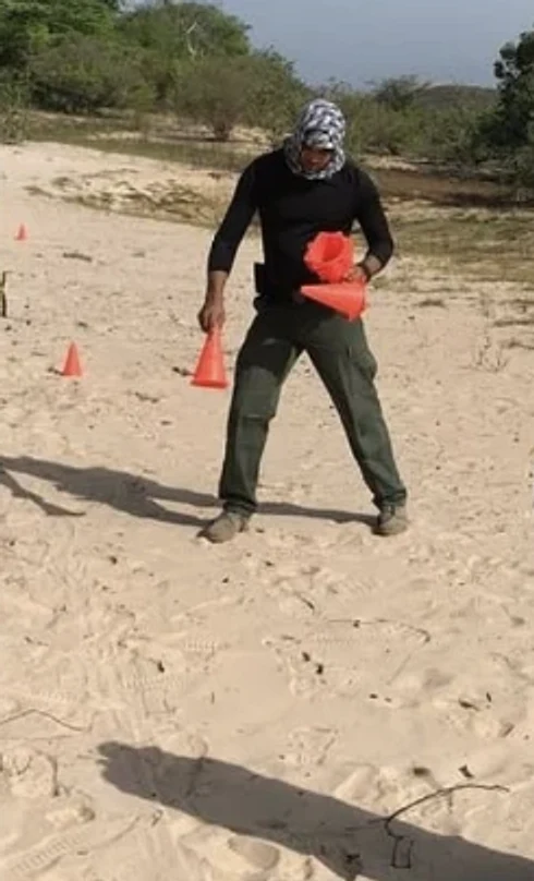 Instrutor montando exercício com cones em campo de areia